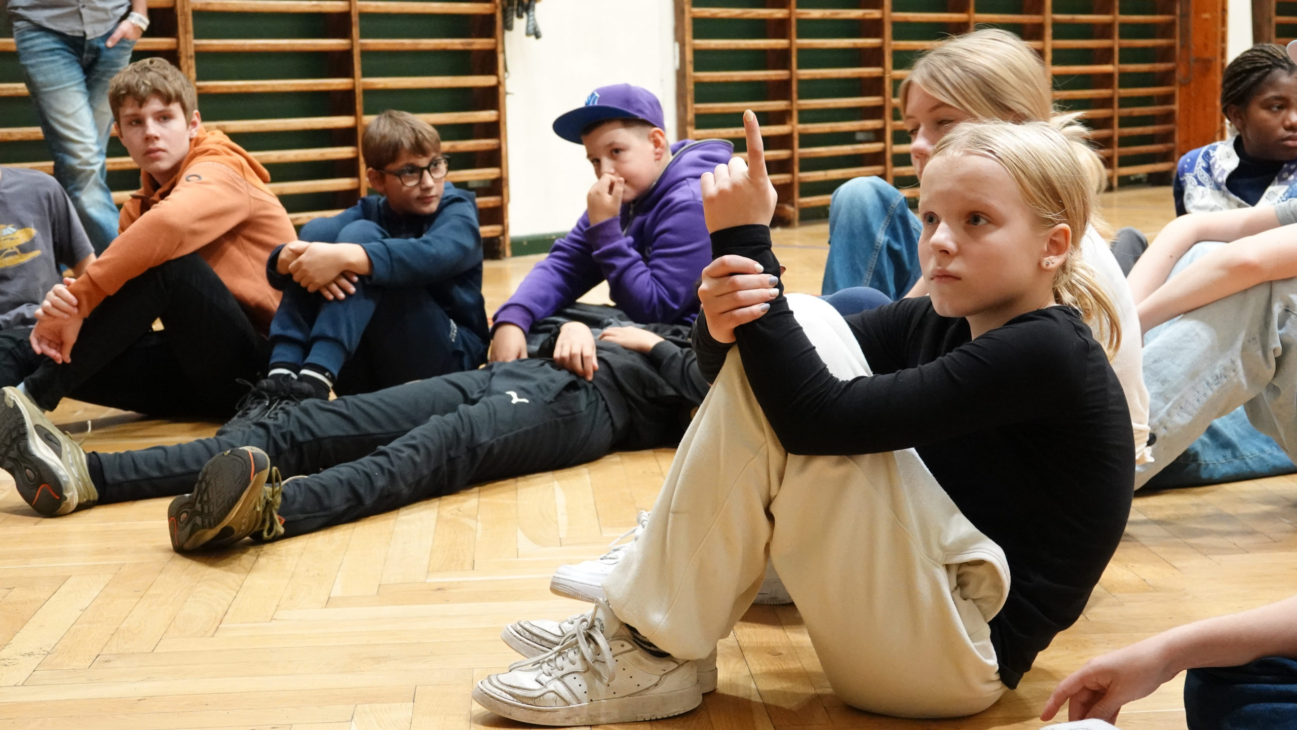 Elever sidder på gulvet i gymnastiksal